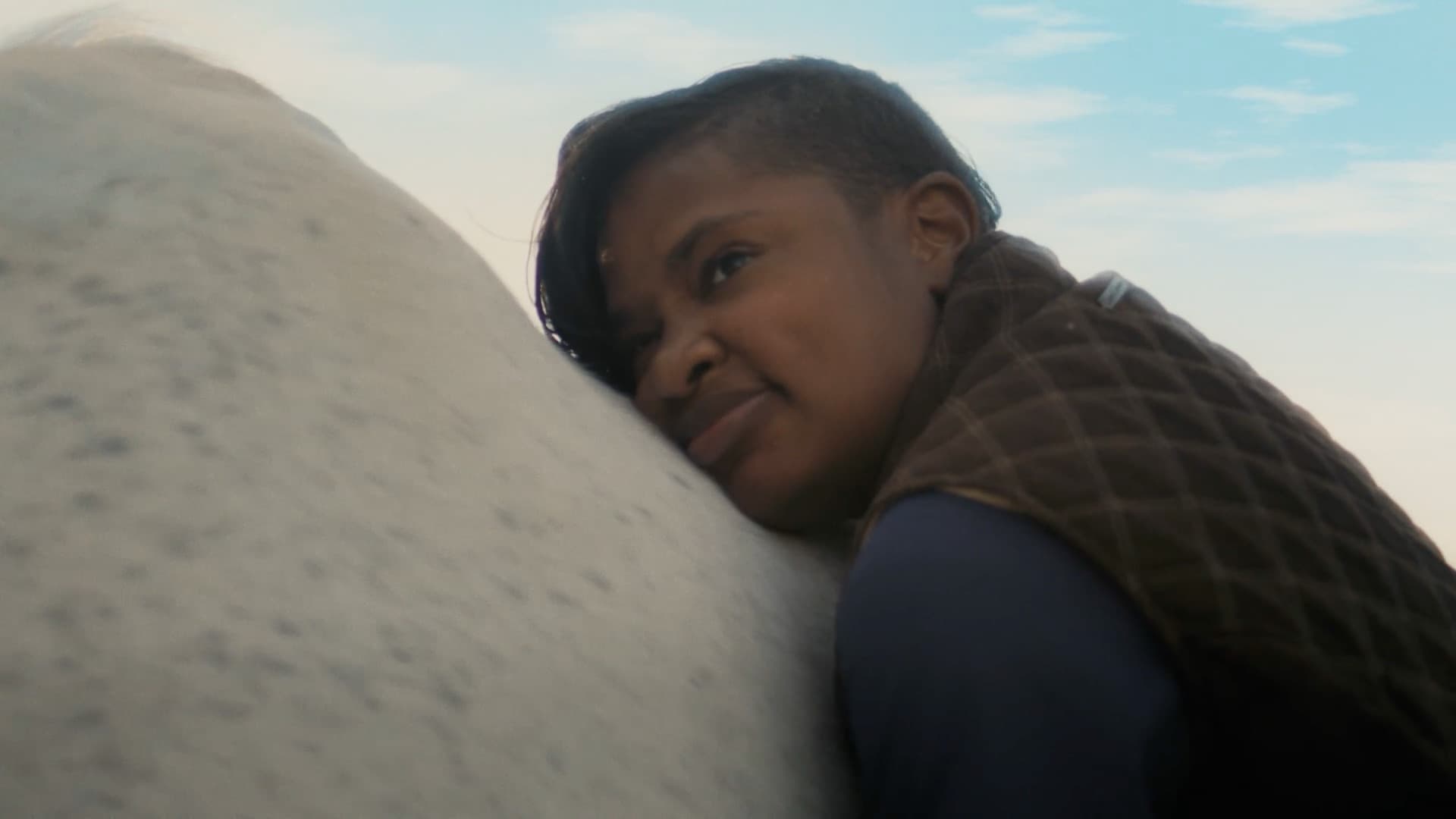 A young girl gazes into the distance beside a horse